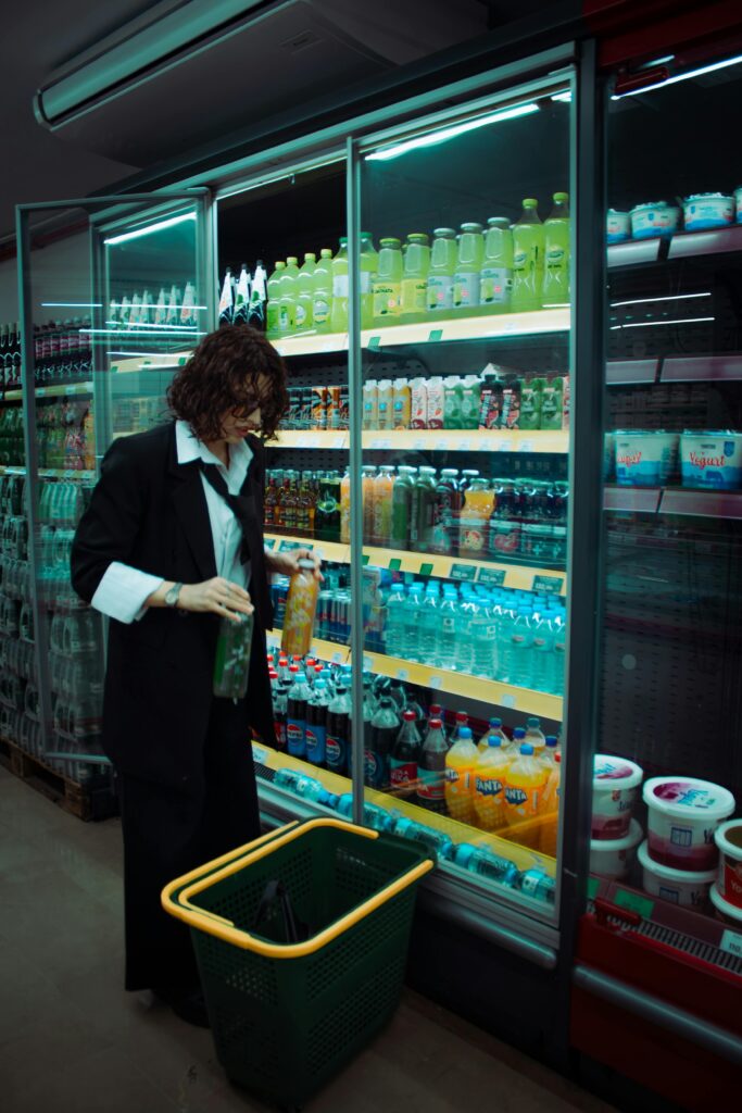 Woman choosing drinks in a grocery store aisle with a shopping basket.